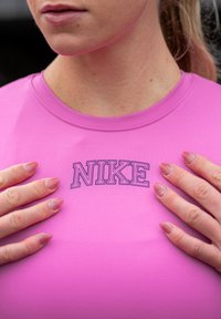 Top atletico aderente rosa con maniche corte; presenta un logo Nike nero sul petto; texture liscia con una finitura leggermente lucida.