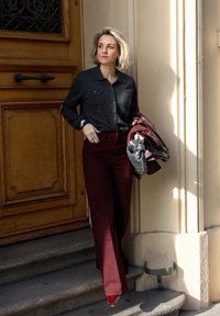 Dark gray button-up shirt with two chest pockets, burgundy high-waisted wide-leg pants, and shiny red pointed shoes, holding a patterned leather bag.