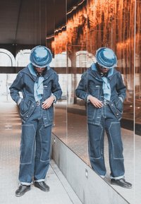 Denim jacket with contrasting stitching, matching loose-fit denim trousers, a light blue scarf, and a wide-brimmed blue hat, reflected in a mirror.