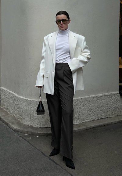 Blazer blanco oversize sobre un suéter de cuello alto blanco, combinado con pantalones anchos oscuros, tacones negros de punta fina y bolso mini negro.