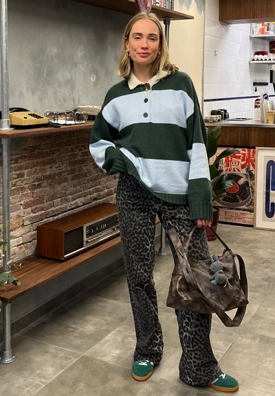 Suéter de punto XL a rayas verde y azul claro con cuello, combinado con pantalones acampanados de estampado de leopardo negro y un bolso marrón con un charm.