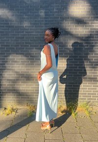 Svetlomodrá saténová šaty s nízkym chrbtom, úzky strih, dlhý dizajn po zem. Nosené s sandálmi na vysokom podpätku so šnúrkami, pred červenou tehlovou stenou.