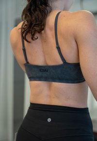 Szürke sportmelltartó állítható pántokkal, puha tapintású és minimális varrásokkal, fekete, magas derekú leggingsszel kombinálva.