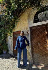 Giacca di denim blu scuro con bottoni, indossata sopra jeans a gamba larga coordinati. Tessuto strutturato con vita aderente e maniche svasate.