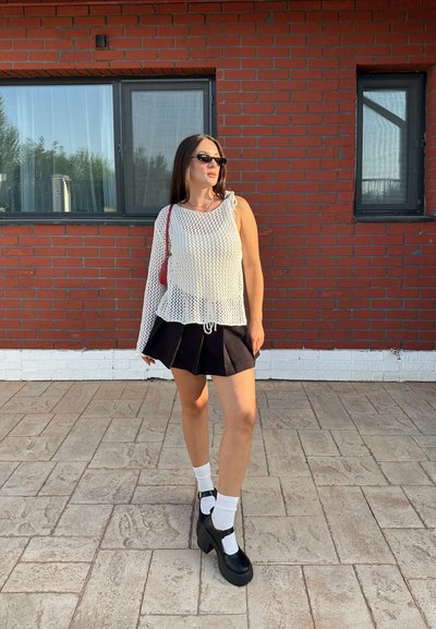 Blusa de punto blanca con tejido abierto, falda negra con pliegues, zapatos de plataforma negros y calcetines tobilleros blancos. Un bolso rojo y gafas de sol completan el look.