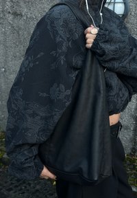 Black padded jacket adorned with textured floral patterns, teamed with a black leather bag. The design boasts loose sleeves and a relaxed fit.