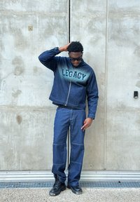 Giacca di jeans con grafica "LEGACY", abbinata a pantaloni di jeans a righe. Stivali da combattimento neri. Il design presenta una chiusura con zip e una vestibilità comoda.