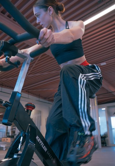 Bicicleta estática en negro con acentos rojos, que cuenta con un marco robusto, manillares ajustables y un ciclista en ropa deportiva, concentrado en pedalear.