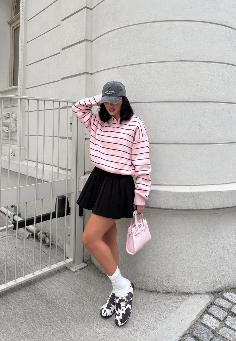 Light pink, striped oversized pullover, black pleated skirt, white socks, cow-print clogs, small pink handbag, grey cap. Urban setting.