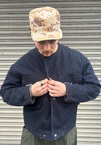 Sötét farmerdzseki lekerekített gallérral, elöl patentzárral �és kontrasztos kockás béléssel. Kaméleonmintás sapkával viselve.