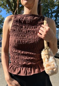 Top marrone con smock e orlo arricciato, caratterizzato da un tessuto testurizzato, abbinato a una borsa in pelliccia sintetica beige e a una tracolla leggera.