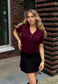 Burgundy short-sleeve top with a v-neck and three buttons, paired with a black skirt. Smooth texture, fitted design, and casual style.