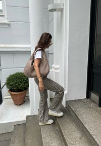 Béžová pletená taška, bílý tričko, šedé kalhoty s rozšířenými nohavicemi s tečkami a bílé tenisky na platformě, na kamenných schodech poblíž květináče.