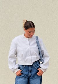 Giacca bomber grigia tagliata con chiusura frontale a bottoni e polsini a coste, abbinata a jeans in denim a vita alta e una borsa a spalla a pois blu.