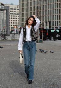 Črn vezenjak preko bele srajce, modri hlače z visokim pasom in črne gležnarje. Nosila je bež torbico. Urbani ozadje.