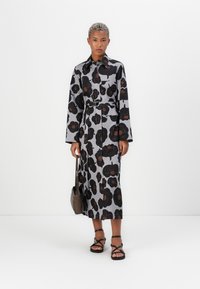 Φλοράλ φόρεμα μίντι σε γκρι, με ζώνη στη μέση, κουμπιά μπροστά και μακριά μανίκια. Συνδυάζεται με μαύρες σανδάλες με λουριά και καφέ τσάντα.