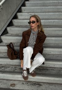 Brown suede oversized jacket, black and white striped top, white jeans, brown trainers, and a brown handbag on the stairs.