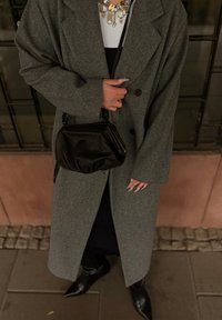 Sivý, nadmerný vlnený kabát s dvojradovým zapínaním. Čierna kožená taška cez rameno. Špičaté čierne topánky na podpätku. Viacvrstvový zlatý náhrdelník ako doplnok.