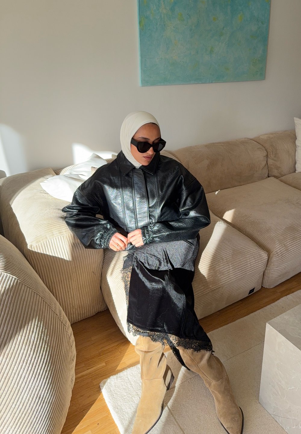 Veste noire en cuir oversize avec manches froncées, associée à une longue robe noire ornée de dentelle et des bottes hautes cognac jusqu'aux genoux.