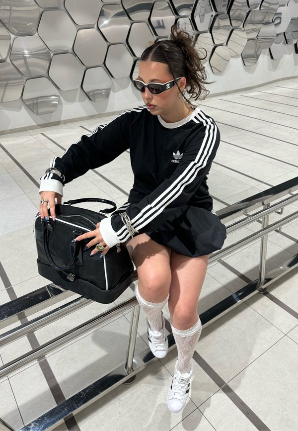 Black long-sleeved shirt with white stripes, black skirt, white knee-high socks, and black handbag. Accessories include rings and sunglasses.