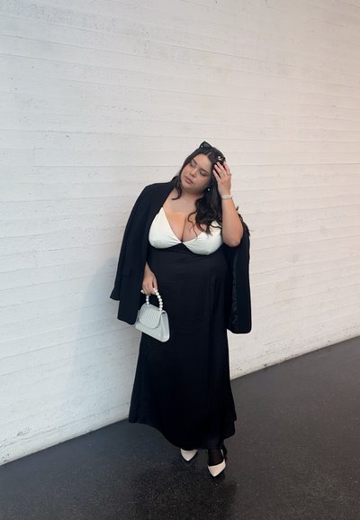 Vestido largo negro con parte superior blanca, americana negra y bolso gris claro con acentos de perlas. Los zapatos de tacón negros completan el conjunto.