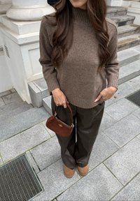 Rjav pleten pulover z visokim ovratnikom, v kombinaciji z ohlapnimi temnorjavimi hlačami. Drži majhno rjavo zamsko torbico. Zamske gležnjarje dopolnjujejo videz.