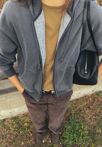 Szara bluza z kapturem i podszewką sherpa, pod spodem oliwkowa koszulka, brązowe spodnie sztruksowe oraz czarna torebka. Widoczne szczegóły swobodnego stroju.