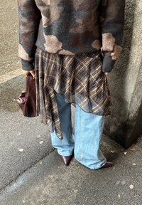 Asymmetrisk ternet nederdel i mørke toner lagdelt over blå, vidde jeans, kombineret med spidse bordeaux hæle og en matchende håndtaske.