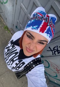 Berretto lavorato a maglia nei colori blu, rosso e bianco, con un design della Union Jack e lettering nero prominente. Camicia bianca con collo nero e borchie.