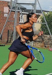 Egy fekete sport crop topot és tengerészkék szoknyát viselő személy fut egy zöld teniszpályán, kék teniszütőt tartva a kezében.