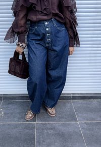 Blugi din denim albastru, cu talie înaltă și croială lejeră, cu cinci nasturi. Geantă din blană sintetică neagră. Pantofi cu imprimeu leopard, bluză transparentă cu mâneci lungi.