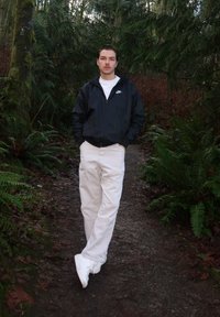 Coupe-vent Nike noir, t-shirt blanc, pantalon cargo beige et baskets blanches. Debout sur un sentier de terre entouré de feuillage vert.