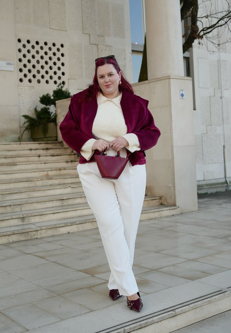 Red faux suede oversized jacket, cream textured sweater, white wide-leg trousers, and burgundy mini handbag. Pointed shoes with embellishments.