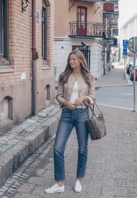 Beige cropped jakke, hvit topp, høyderte blå jeans, hvite joggesko og grå totebag. Fortausmiljø med murbygninger.