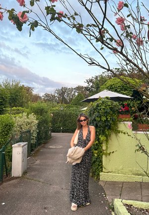 Vestido maxi con un estampado floral en blanco y negro. La tela se drapea elegantemente, complementado con sandalias de plataforma blancas y un chal gris claro.