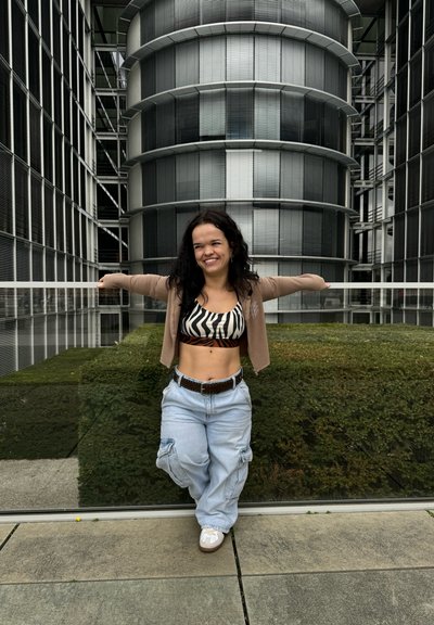 Conjunto casual que incluye un top corto a rayas, un cárdigan beige y pantalones cargo azules holgados. Zapatillas blancas completan el look con un fondo urbano.