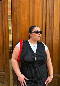Vestido preto riscas com botões, combinado com uma t-shirt branca. Acessórios incluem uma mala vermelha e óculos de sol. Fundo de madeira.