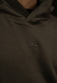 P hoodie verde oliva feito de uma mistura de algodão macio, apresentando um logo bordado tonal no peito. Design simples com um corte descontraído.