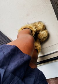 Zapatillas de felpa con un exterior esponjoso de color marrón claro, llevadas con una prenda de color azul oscuro, situadas sobre una superficie texturizada.