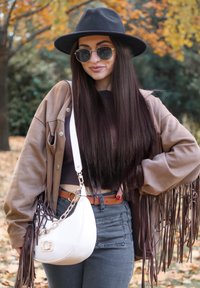 Bruine jack met franjes over een donker topje, grijze jeans met hoge taille, handtas met witte kettingdetail, ronde zonnebril en een zwarte vilten hoed.