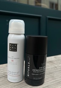 Skummande duschgel i en vit cylindrisk flaska, 50 ml, bredvid en svart antiperspirantstick, 75 ml, båda från Rituals.