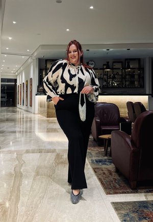 Blusa a rayas en blanco y negro con mangas abullonadas, pantalones anchos negros y zapatos con estampado, sosteniendo un bolso brillante en un entorno moderno.