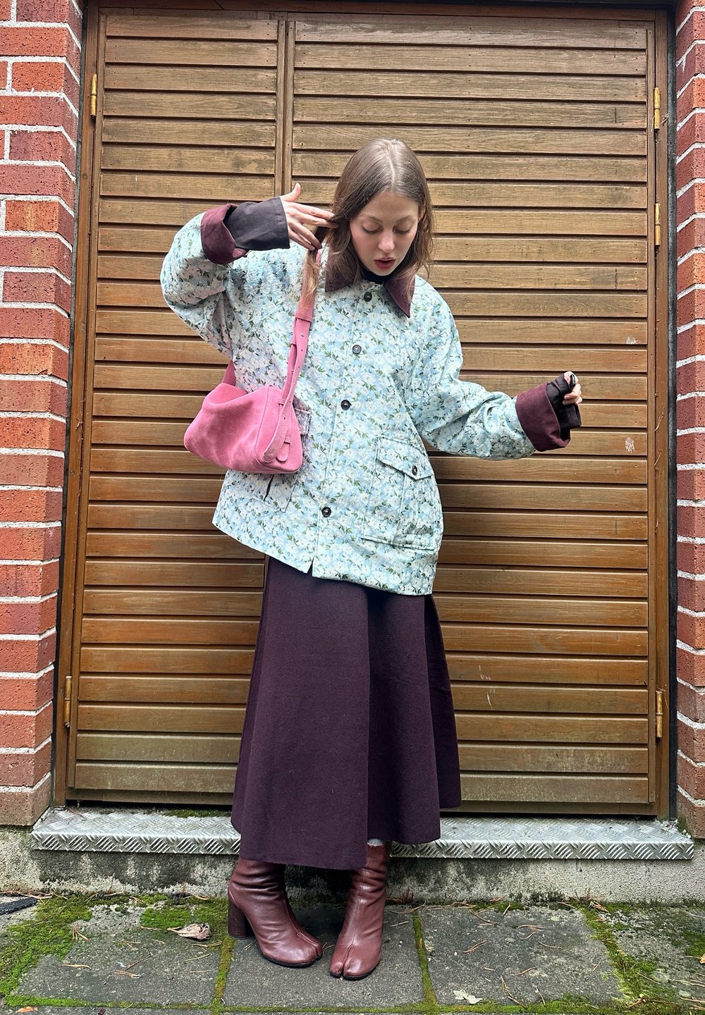 Ljusblå vadderad jacka med blommönster, bruna muddar, lång mörk kjol och rosa handväska. Bärs med bruna stövlar med klack.