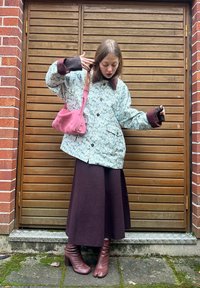 Ljusblå vadderad jacka med blommönster, bruna muddar, lång mörk kjol och rosa handväska. Bärs med bruna stövlar med klack.