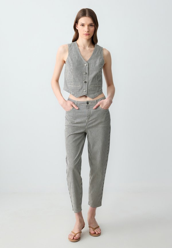 Un gilet court rayé gris et blanc avec des boutons associé à un pantalon ajusté assorti. Le modèle porte des sandales plates au design minimaliste.