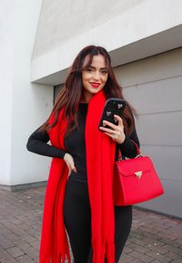 Écharpe en laine rouge, haut ajusté à manches longues noir, et un sac à main structuré rouge avec un fermoir doré. Smartphone avec des accents en forme de cœur à la main.