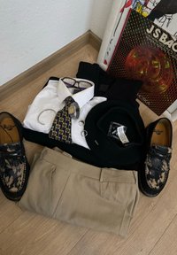 Sort baret, hvid skjorte, mønstret slips, sort sweater, beige bukser, briller, sølvur, sorte sko med mønster, ringe og smykker.