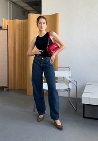 Musthave mustat ilmaõlapaeltega top, kõrge vöökohtadega tume denim teksad, punane käekott keerdunud rihmaga ja pruunid teravatooted kontsad hallil põrandal.