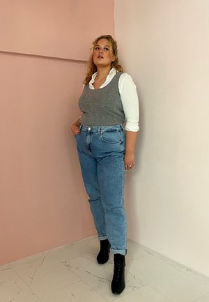 Top de punto gris sobre una camisa blanca con cuello, combinado con unos vaqueros de cintura alta de color azul claro y botas de tobillo negras con cordones.