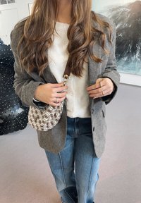 Grey herringbone blazer, white button-up shirt, blue jeans, and a patterned brown and cream shoulder bag with a brown strap.